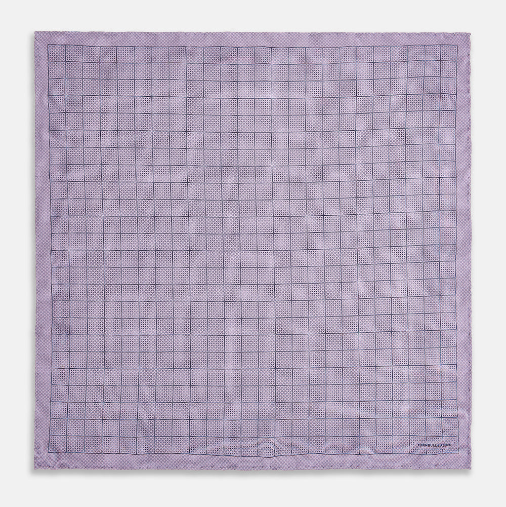 The Checked Lilac Pocket Square in Silk by Turnbull & Asser UK features a grid pattern in purple with a solid border, neatly folded to display its double-sided design and contrasting black and white dotted squares on the reverse side.