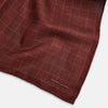 View 3 of product The Turnbull & Asser UK Checked Burgundy Pocket Square in Silk features a sophisticated burgundy hue with a subtle grid pattern. It's displayed folded at one corner to reveal a contrasting small checkered design on the reverse, showcasing its refined double-sided craftsmanship.