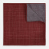 View 4 of product The Turnbull & Asser UK Checked Burgundy Pocket Square in Silk features a sophisticated burgundy hue with a subtle grid pattern. It's displayed folded at one corner to reveal a contrasting small checkered design on the reverse, showcasing its refined double-sided craftsmanship.