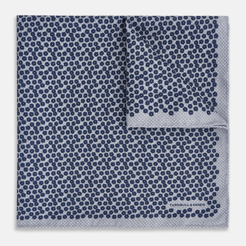 The Turnbull & Asser UK Floral Blue Pocket Square in Silk showcases a refined double-sided design, with a clustered dot pattern in blue and white on the front and a delicate fine dotted motif on the back. Presented with one corner elegantly folded, it exudes sophisticated style.