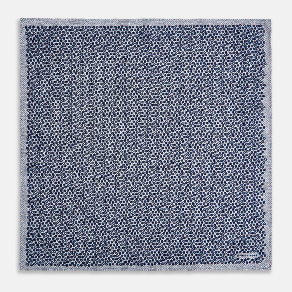 The Turnbull & Asser UK Floral Blue Pocket Square in Silk showcases a refined double-sided design, with a clustered dot pattern in blue and white on the front and a delicate fine dotted motif on the back. Presented with one corner elegantly folded, it exudes sophisticated style.