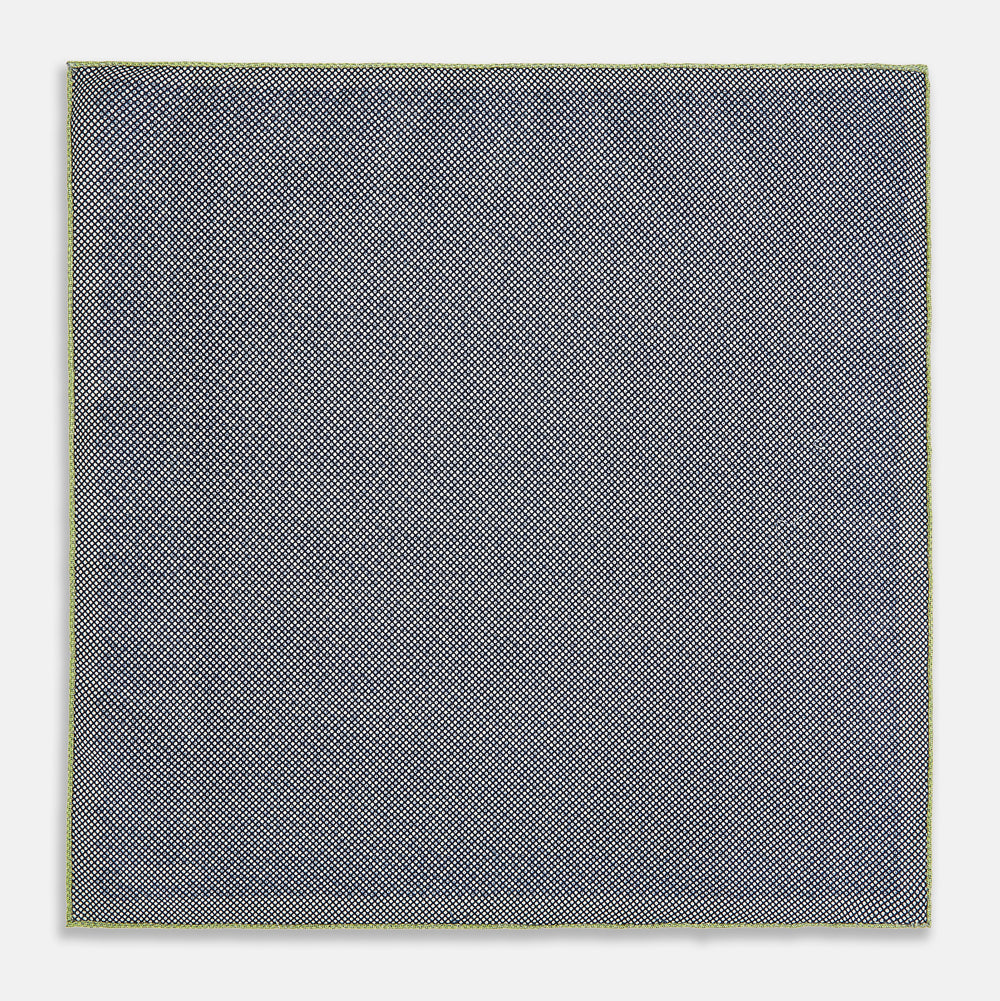 The Turnbull & Asser UK Floral Green Pocket Square in Silk is a square accessory featuring a blue floral pattern with a green border, partly folded at one corner to showcase its double-sided design, revealing a navy and light green dotted pattern on the reverse.