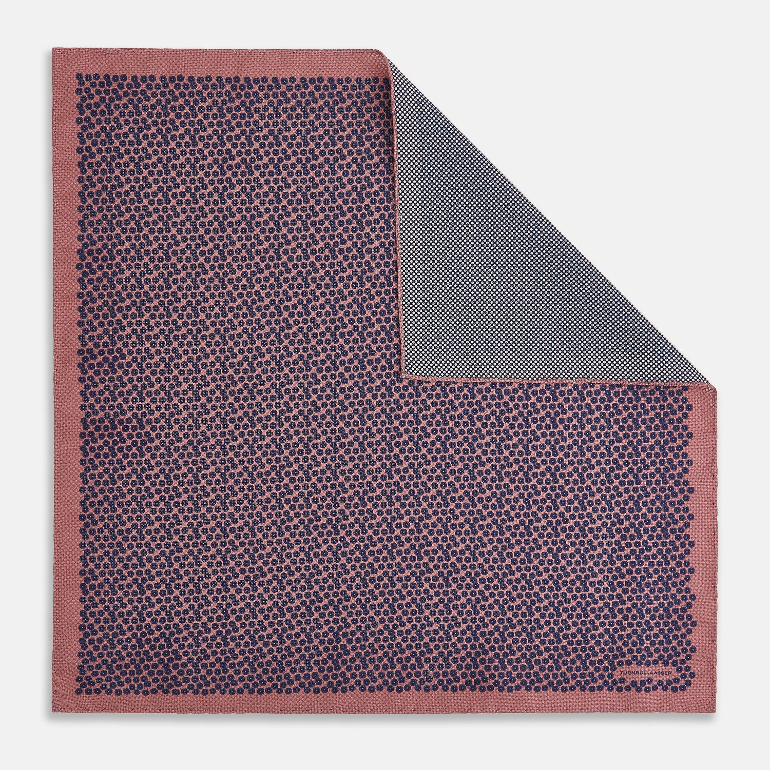 View 1 of product The Floral Pink Pocket Square in Silk by Turnbull & Asser UK showcases a refined pattern with a pink floral design and a contrasting border. The top right corner is elegantly folded to reveal the reverse side’s complementary blue and white dotted motif, emphasizing its double-sided versatility.
