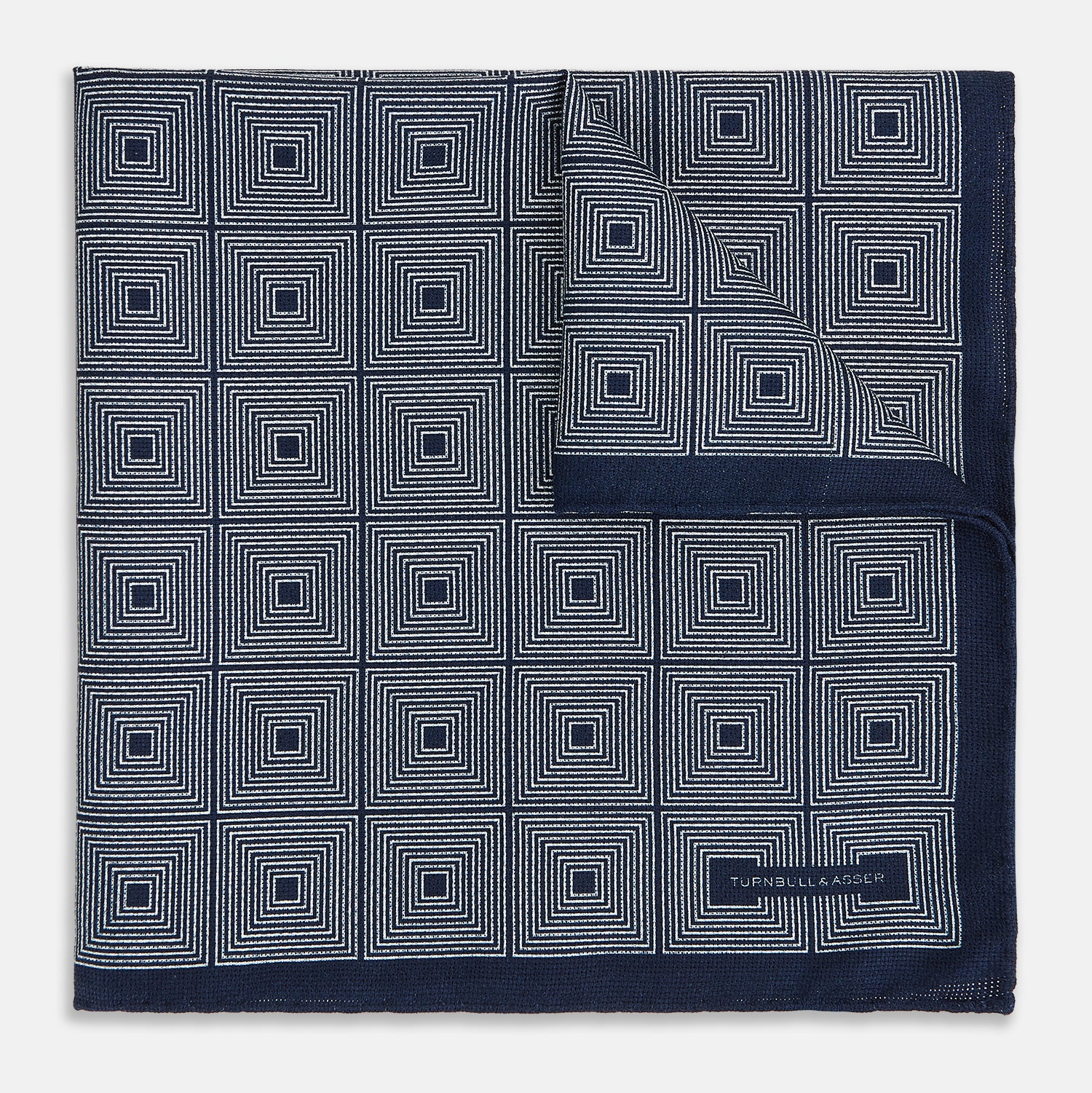 View 2 of product Introducing the Geometric Navy Tile Pocket Square in Silk by Turnbull & Asser UK—a folded navy and white accessory showcasing a double-sided design, with one side featuring concentric squares that form a striking geometric pattern and the other adorned with an elegant small dot motif.