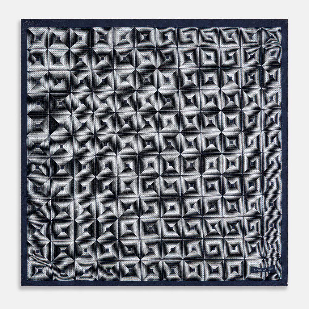 Introducing the Geometric Navy Tile Pocket Square in Silk by Turnbull & Asser UK—a folded navy and white accessory showcasing a double-sided design, with one side featuring concentric squares that form a striking geometric pattern and the other adorned with an elegant small dot motif.
