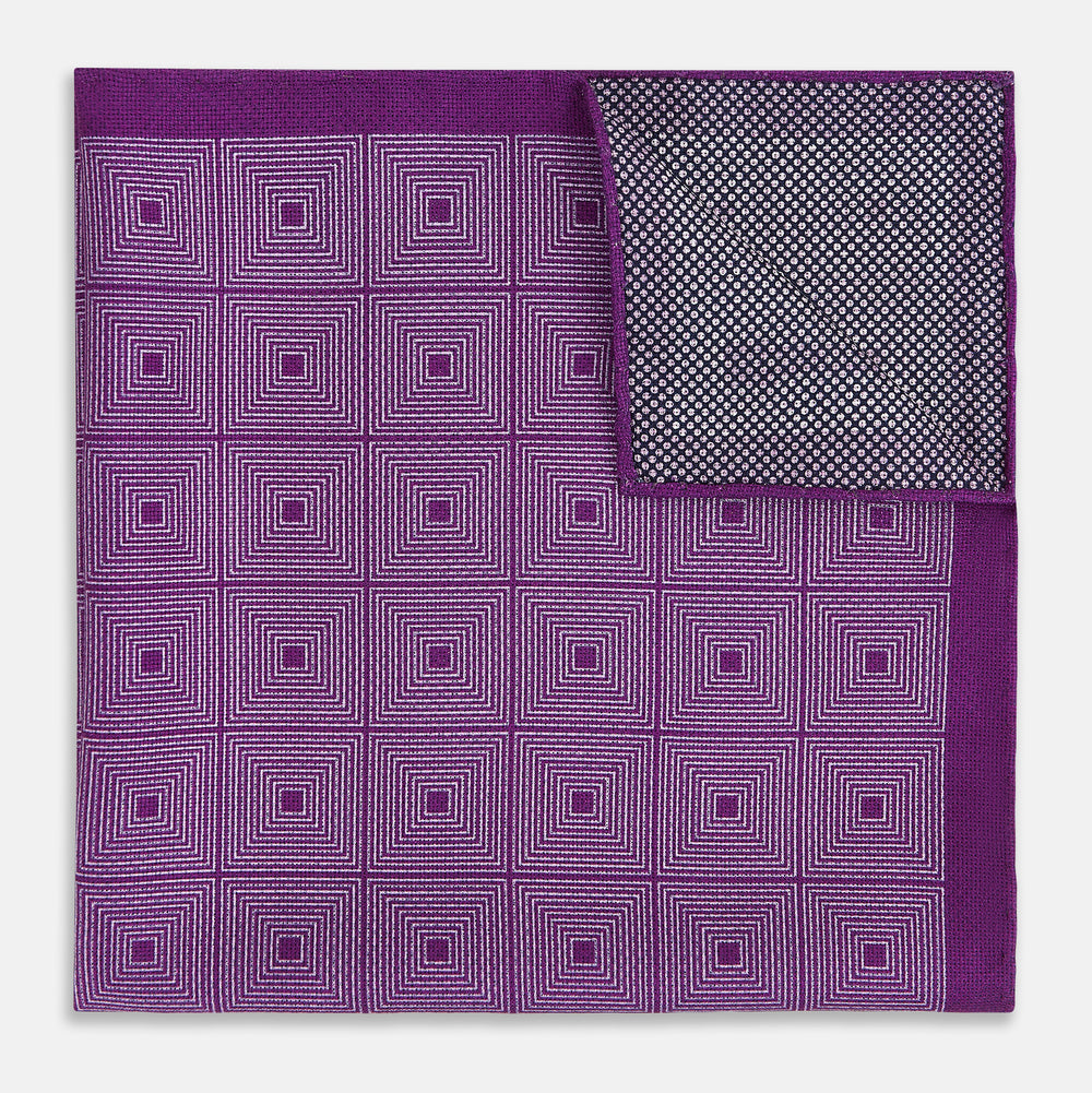 The Turnbull & Asser UK Geometric Purple Tile Pocket Square in Silk features a vibrant purple hue adorned with concentric square motifs. One corner is folded to reveal its double-sided design, showcasing a contrasting black-and-white dotted underside.