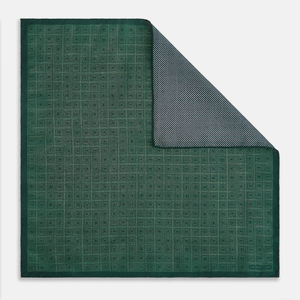 The Geometric Green Tile Pocket Square in Silk by Turnbull & Asser UK features a sophisticated tonal green design with a subtle pattern of concentric squares. One corner is folded to highlight the elegant double-sided construction, revealing a contrasting black and white small dot pattern on the reverse.