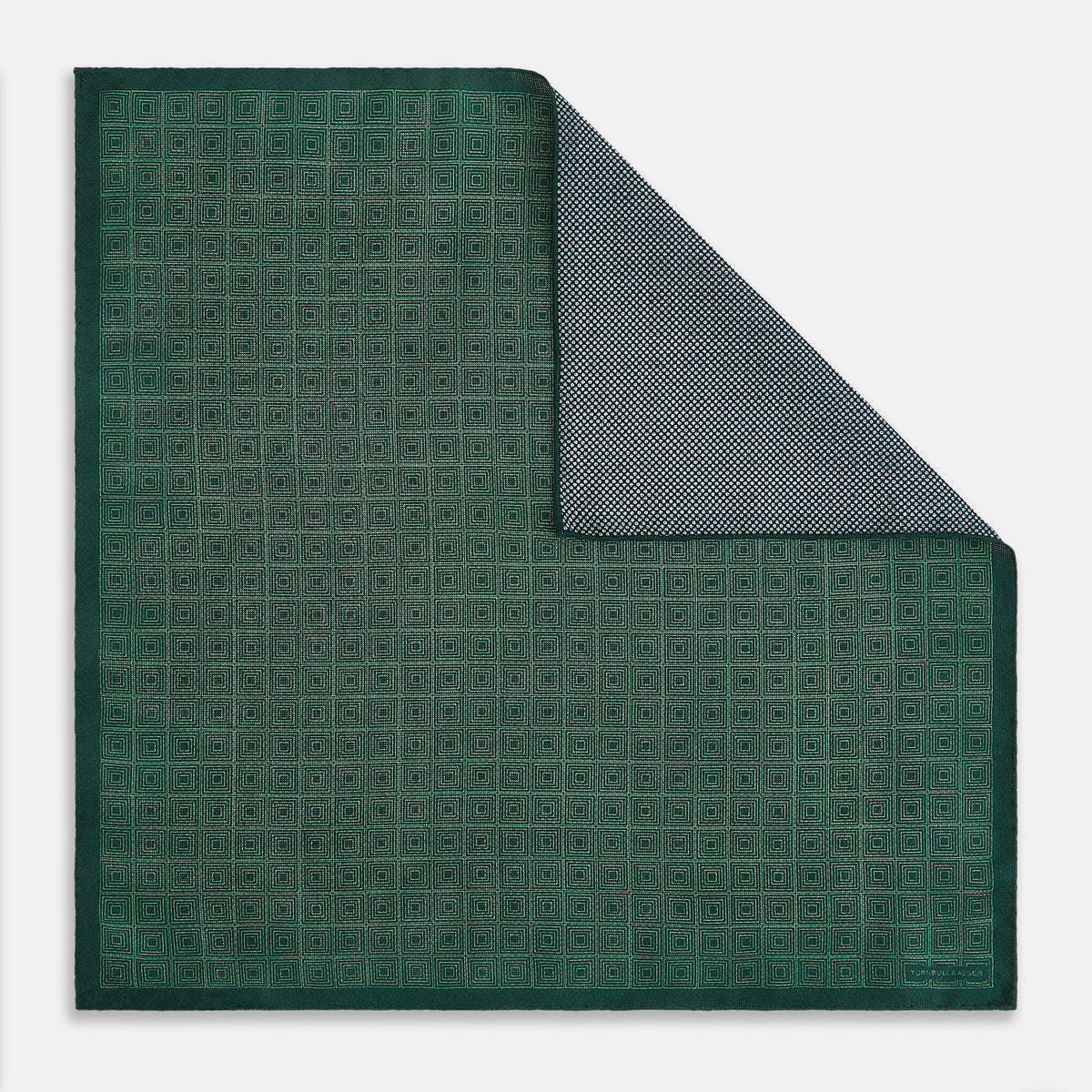 View 3 of product The Geometric Green Tile Pocket Square in Silk by Turnbull & Asser UK features a sophisticated tonal green design with a subtle pattern of concentric squares. One corner is folded to highlight the elegant double-sided construction, revealing a contrasting black and white small dot pattern on the reverse.