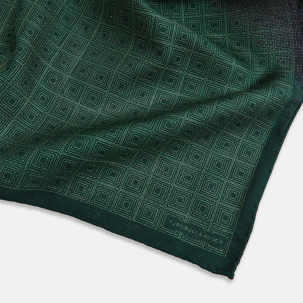 The Geometric Green Tile Pocket Square in Silk by Turnbull & Asser UK features a sophisticated tonal green design with a subtle pattern of concentric squares. One corner is folded to highlight the elegant double-sided construction, revealing a contrasting black and white small dot pattern on the reverse.