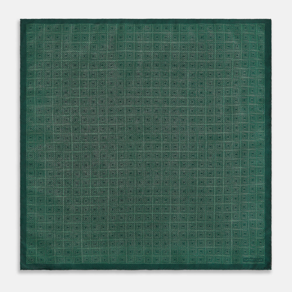 The Geometric Green Tile Pocket Square in Silk by Turnbull & Asser UK features a sophisticated tonal green design with a subtle pattern of concentric squares. One corner is folded to highlight the elegant double-sided construction, revealing a contrasting black and white small dot pattern on the reverse.
