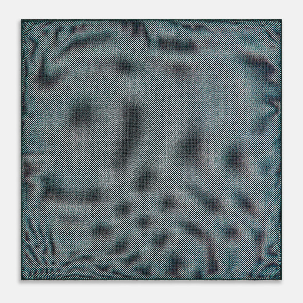 The Geometric Green Tile Pocket Square in Silk by Turnbull & Asser UK features a sophisticated tonal green design with a subtle pattern of concentric squares. One corner is folded to highlight the elegant double-sided construction, revealing a contrasting black and white small dot pattern on the reverse.