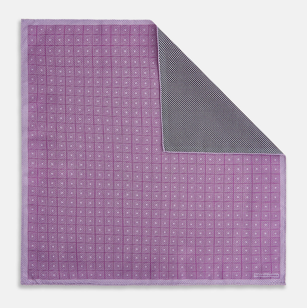 Certainly! Here’s a rewritten version of your sentence, incorporating the product data: The Geometric Lilac Tile Pocket Square in Silk by Turnbull & Asser UK features a lilac purple geometric pattern with a subtle square design, partially folded to reveal its double-sided construction with a contrasting black and white dotted pattern on the reverse.