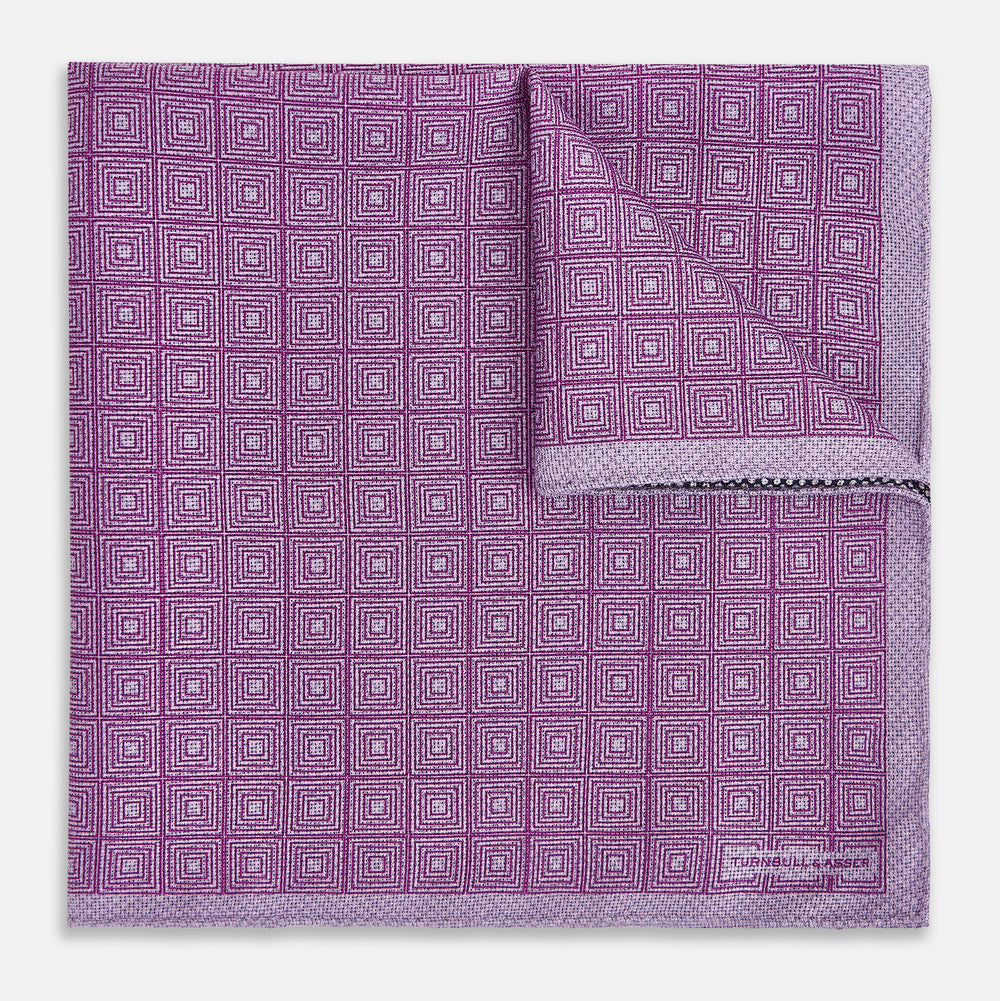 Certainly! Here’s a rewritten version of your sentence, incorporating the product data: The Geometric Lilac Tile Pocket Square in Silk by Turnbull & Asser UK features a lilac purple geometric pattern with a subtle square design, partially folded to reveal its double-sided construction with a contrasting black and white dotted pattern on the reverse.