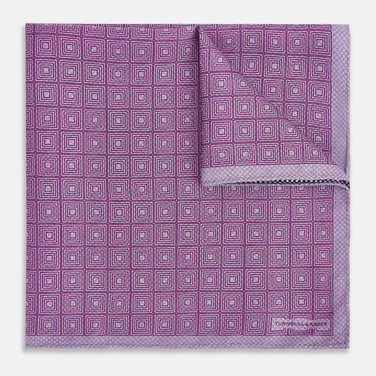 View 2 of product Certainly! Here’s a rewritten version of your sentence, incorporating the product data: The Geometric Lilac Tile Pocket Square in Silk by Turnbull & Asser UK features a lilac purple geometric pattern with a subtle square design, partially folded to reveal its double-sided construction with a contrasting black and white dotted pattern on the reverse.