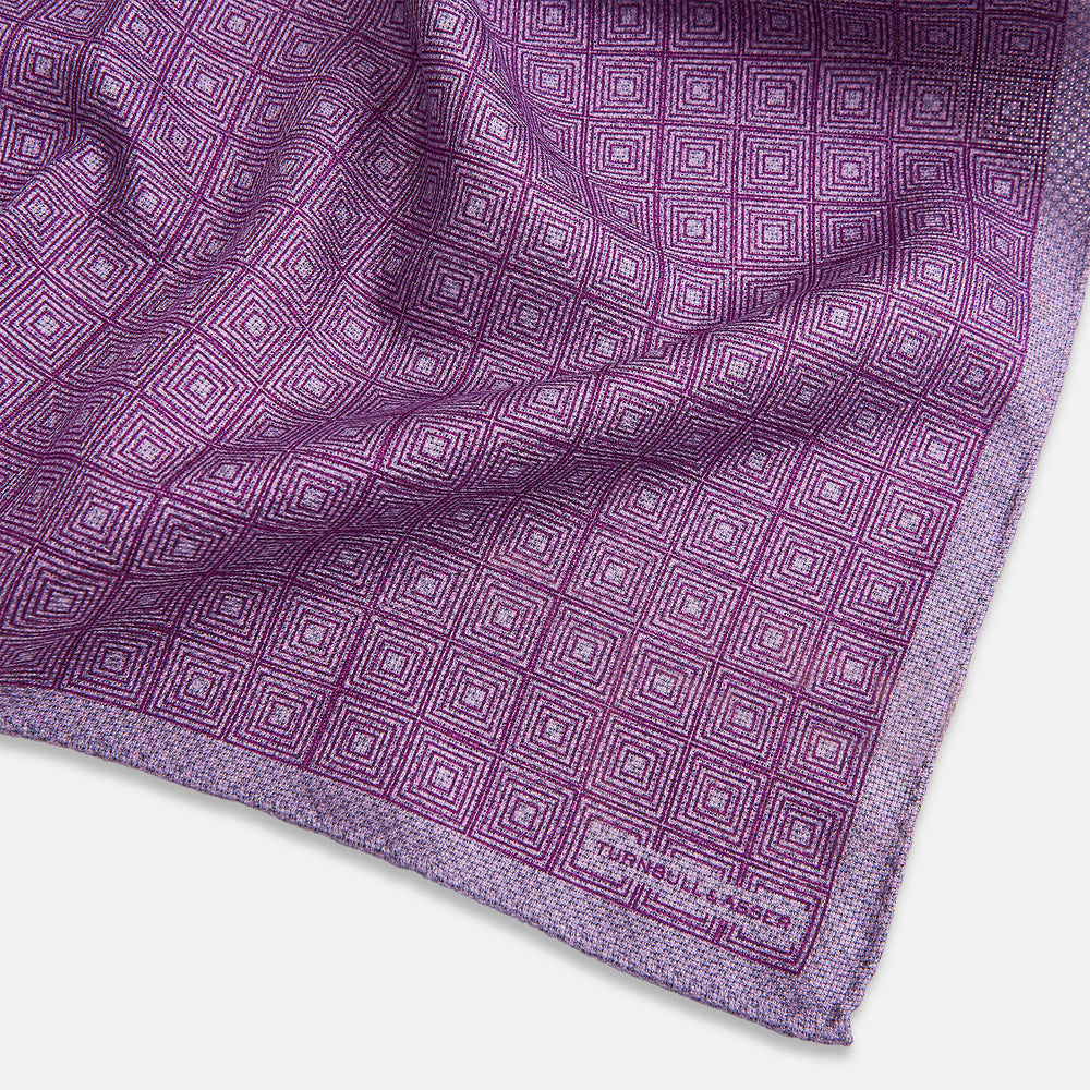 Certainly! Here’s a rewritten version of your sentence, incorporating the product data: The Geometric Lilac Tile Pocket Square in Silk by Turnbull & Asser UK features a lilac purple geometric pattern with a subtle square design, partially folded to reveal its double-sided construction with a contrasting black and white dotted pattern on the reverse.