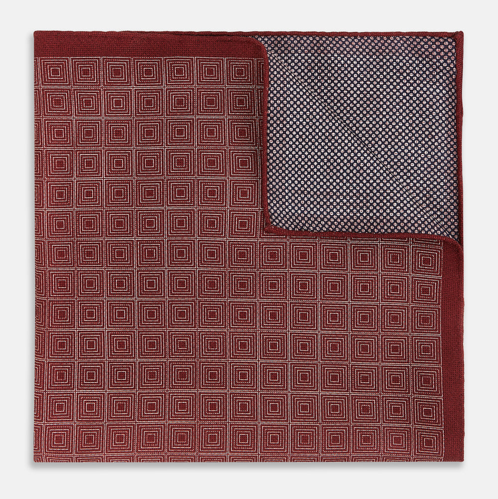 The Turnbull & Asser UK Geometric Burgundy Tile Pocket Square in Silk is displayed partly folded, showcasing its bold geometric grid pattern with concentric burgundy squares on the front and a contrasting black-and-white dotted design on the reverse.