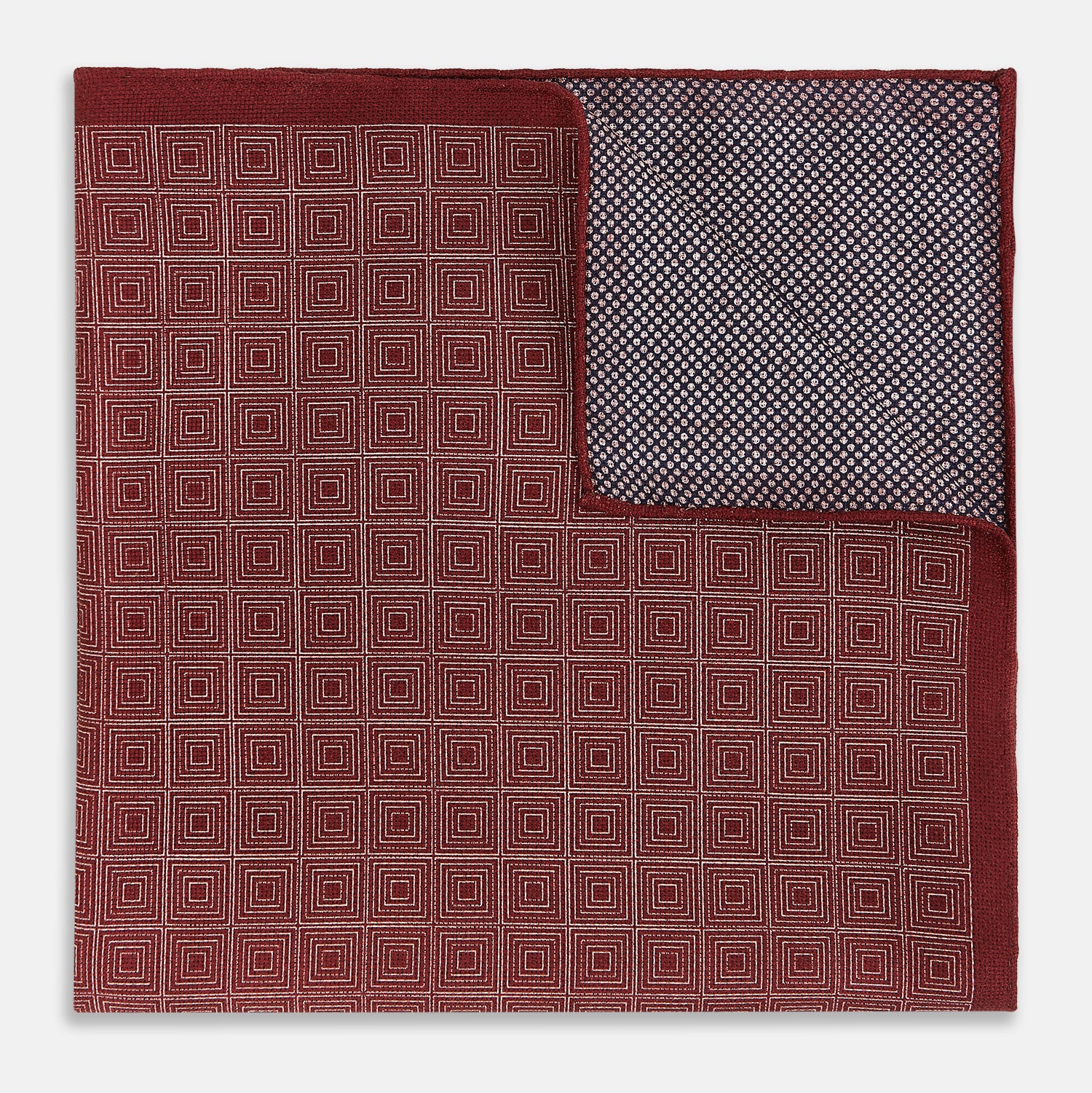 View 2 of product The Turnbull & Asser UK Geometric Burgundy Tile Pocket Square in Silk is displayed partly folded, showcasing its bold geometric grid pattern with concentric burgundy squares on the front and a contrasting black-and-white dotted design on the reverse.