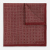 View 4 of product The Turnbull & Asser UK Geometric Burgundy Tile Pocket Square in Silk is displayed partly folded, showcasing its bold geometric grid pattern with concentric burgundy squares on the front and a contrasting black-and-white dotted design on the reverse.