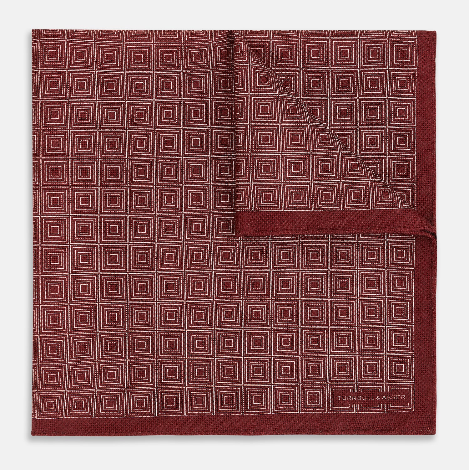 View 4 of product The Turnbull & Asser UK Geometric Burgundy Tile Pocket Square in Silk is displayed partly folded, showcasing its bold geometric grid pattern with concentric burgundy squares on the front and a contrasting black-and-white dotted design on the reverse.