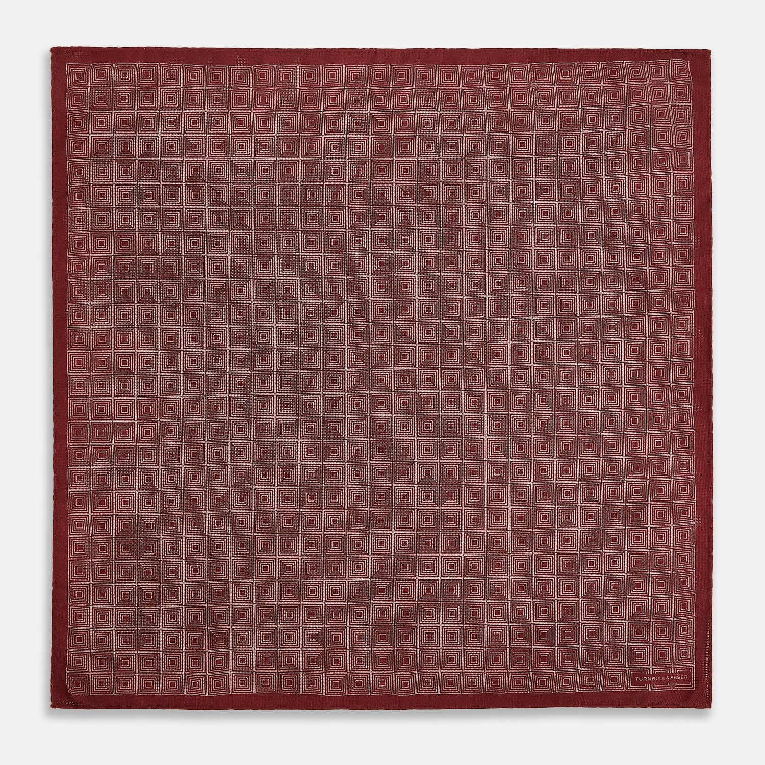 View 5 of product The Turnbull & Asser UK Geometric Burgundy Tile Pocket Square in Silk is displayed partly folded, showcasing its bold geometric grid pattern with concentric burgundy squares on the front and a contrasting black-and-white dotted design on the reverse.