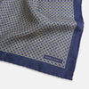 View 3 of product The Geometric Blue Pocket Square in Silk from Turnbull & Asser UK showcases a blue border and double-sided design, with a geometric pattern at the center. A folded corner reveals a refined, tighter dot motif on the reverse side, emphasizing the intricate craftsmanship of this finely woven accessory.