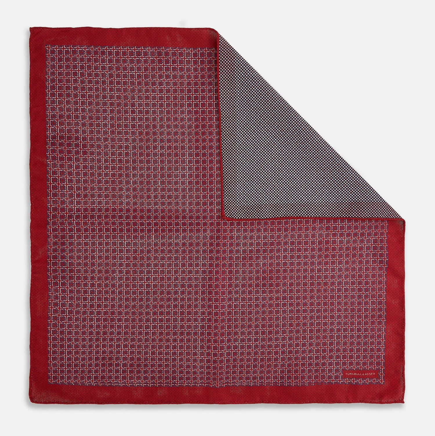 View 1 of product Turnbull & Asser UK’s Geometric Red Pocket Square in Silk features a small white checkered pattern and a cleverly flipped corner to showcase its contrasting black and white micro-dot reverse design.