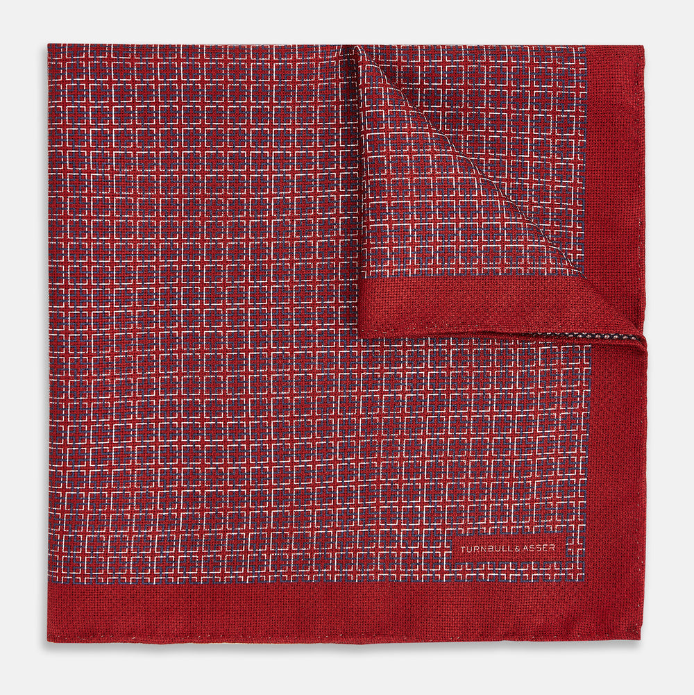 Turnbull & Asser UK’s Geometric Red Pocket Square in Silk features a small white checkered pattern and a cleverly flipped corner to showcase its contrasting black and white micro-dot reverse design.