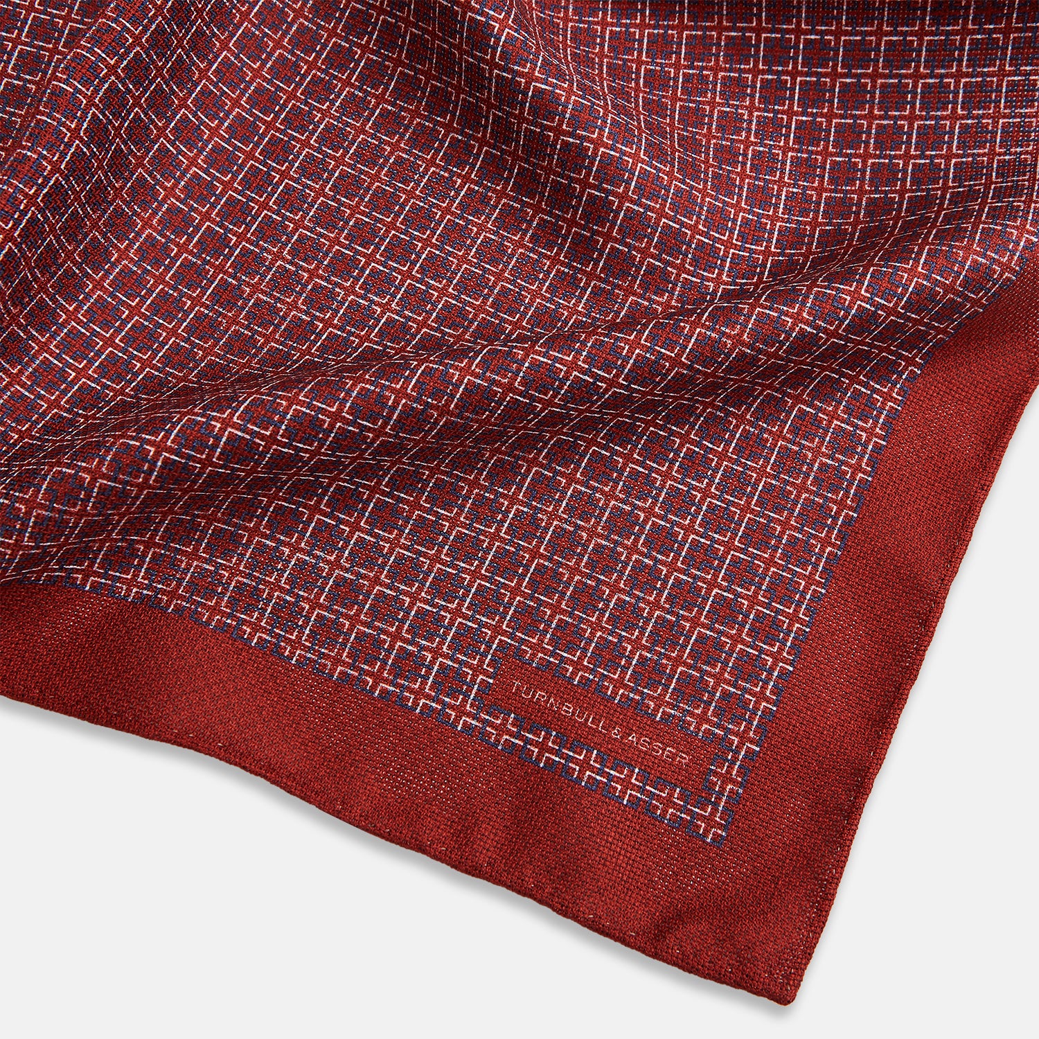 View 3 of product Turnbull & Asser UK’s Geometric Red Pocket Square in Silk features a small white checkered pattern and a cleverly flipped corner to showcase its contrasting black and white micro-dot reverse design.