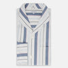View 5 of product The Turnbull & Asser Blue Blazer Stripe Pyjama Shirt features a collar, chest pocket, and vertical blue, white, and light red stripes—an elegant long-sleeve loungewear piece neatly displayed on a plain white background.