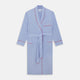 The Turnbull & Asser Light Blue Piped End-On-End Cotton Gown features a belted waist, three front pockets, and red piping on the collar, pockets, and cuffs—ideal for travel. Displayed against a white background.
