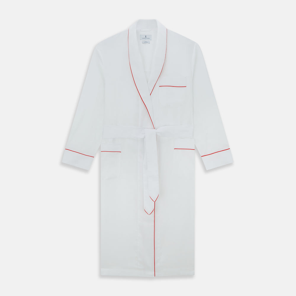 The Turnbull & Asser White Piped Herringbone Cotton Gown features long sleeves, a waist tie, chest pocket, and striking red piping on the collar, cuffs, pocket, and edges—an elegant piece showcased against a white background.
