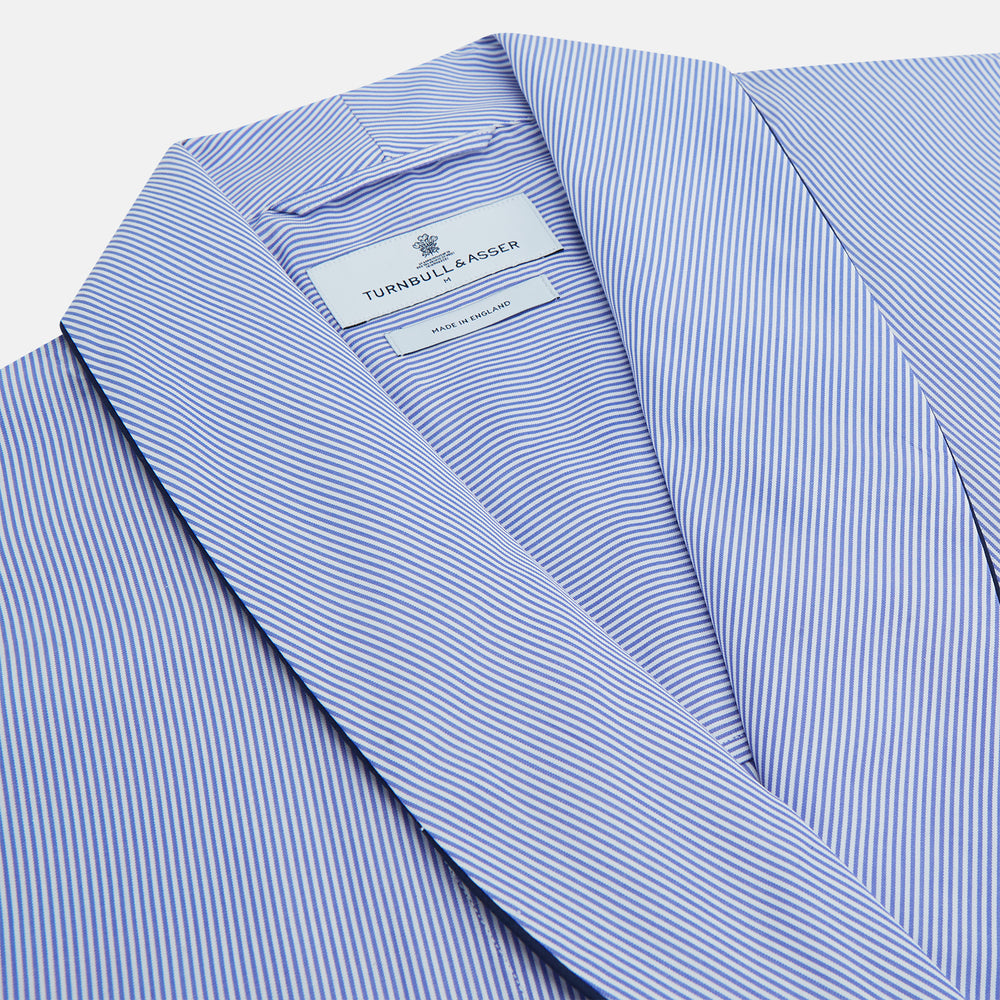 The Blue Fine Bengal Stripe Piped Cotton Gown by Turnbull & Asser features long sleeves, a shawl collar, navy piping, three pockets, and a fabric belt—ideal for those who appreciate classic cotton dressing gowns.