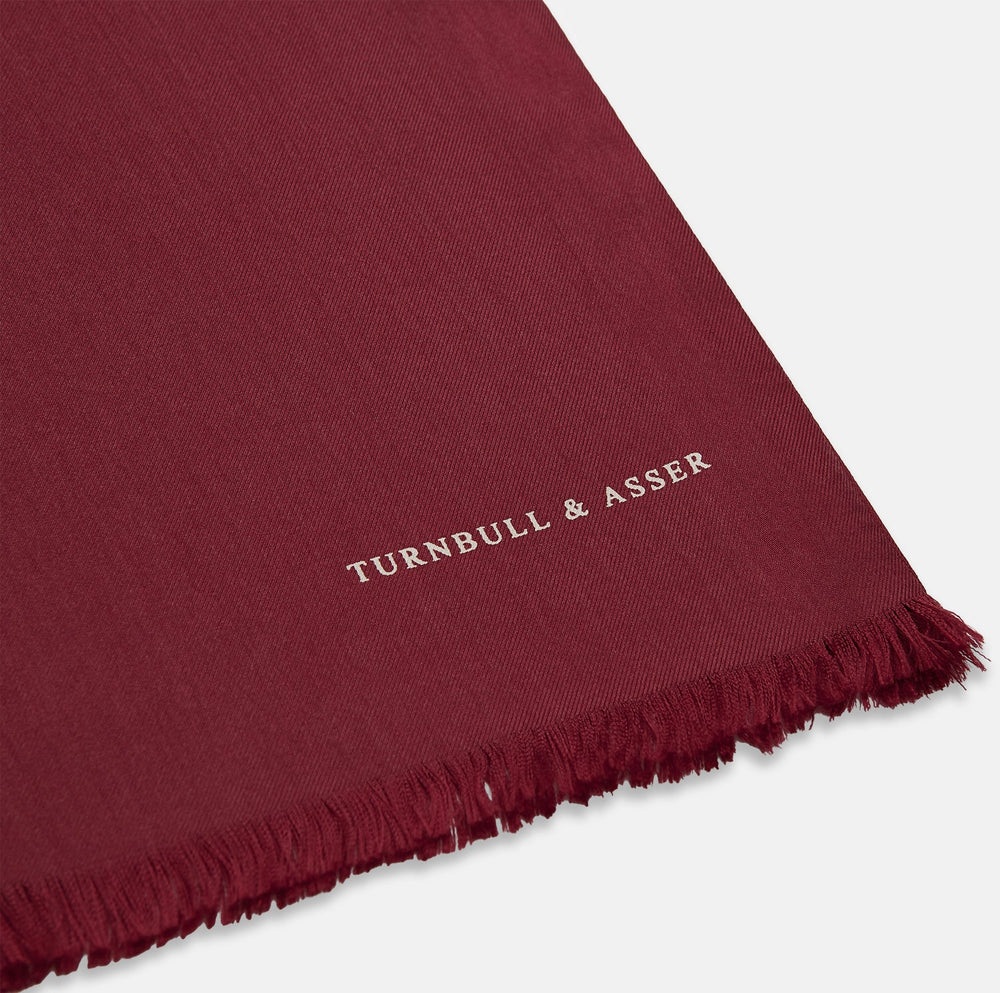 The Plain Wine Silk Scarf by Turnbull & Asser is a long, smooth accessory with subtle fringe and white Turnbull & Asser embroidery on one corner. It comes neatly folded in a deep wine color, perfect for an elegant touch.
