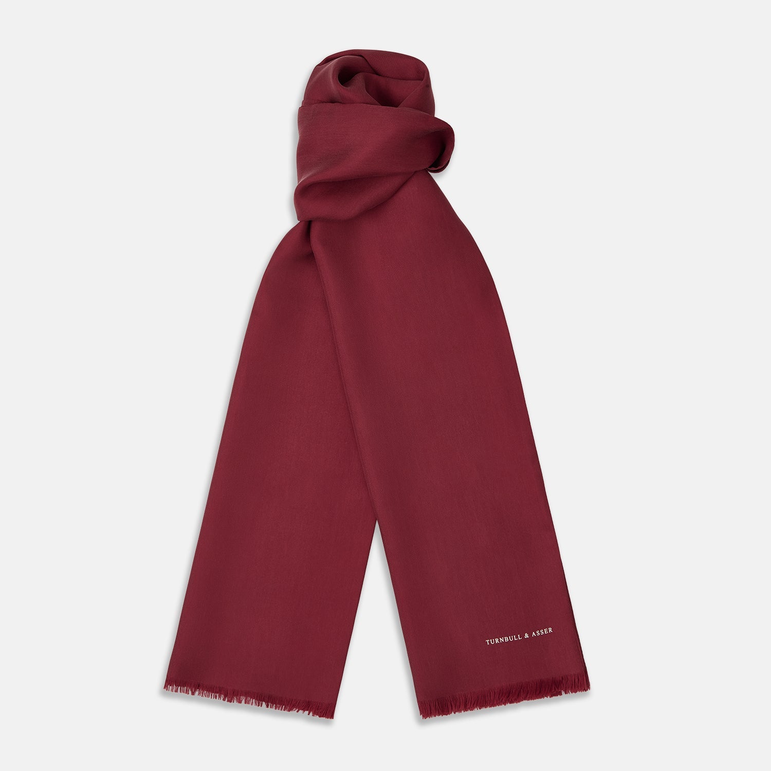 View 1 of product The Plain Wine Silk Scarf by Turnbull & Asser is a long, smooth accessory with subtle fringe and white Turnbull & Asser embroidery on one corner. It comes neatly folded in a deep wine color, perfect for an elegant touch.