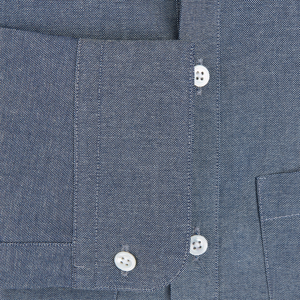 The Turnbull & Asser Steel Blue Piccadilly Shirt features long sleeves, a button-up front, two chest pockets, and white buttons, shown against a plain white background.