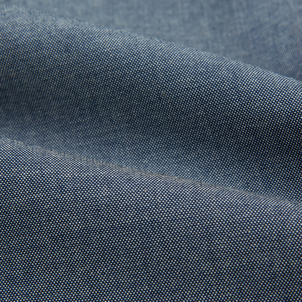 The Turnbull & Asser Steel Blue Piccadilly Shirt features long sleeves, a button-up front, two chest pockets, and white buttons, shown against a plain white background.