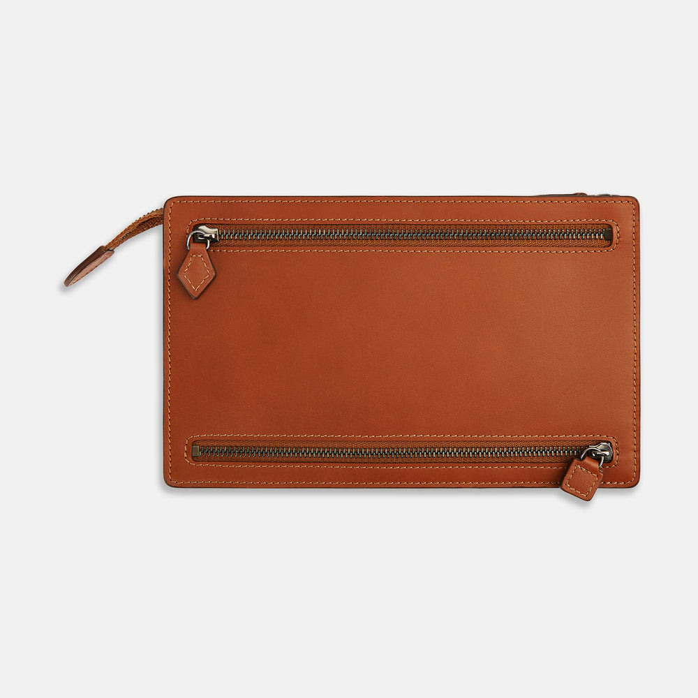 The Cognac Leather Zip Envelope Pouch by Turnbull & Asser UK features two horizontal zippered pockets, stitched edges, and leather pulls—offering a stylish way to organize essentials when you travel.