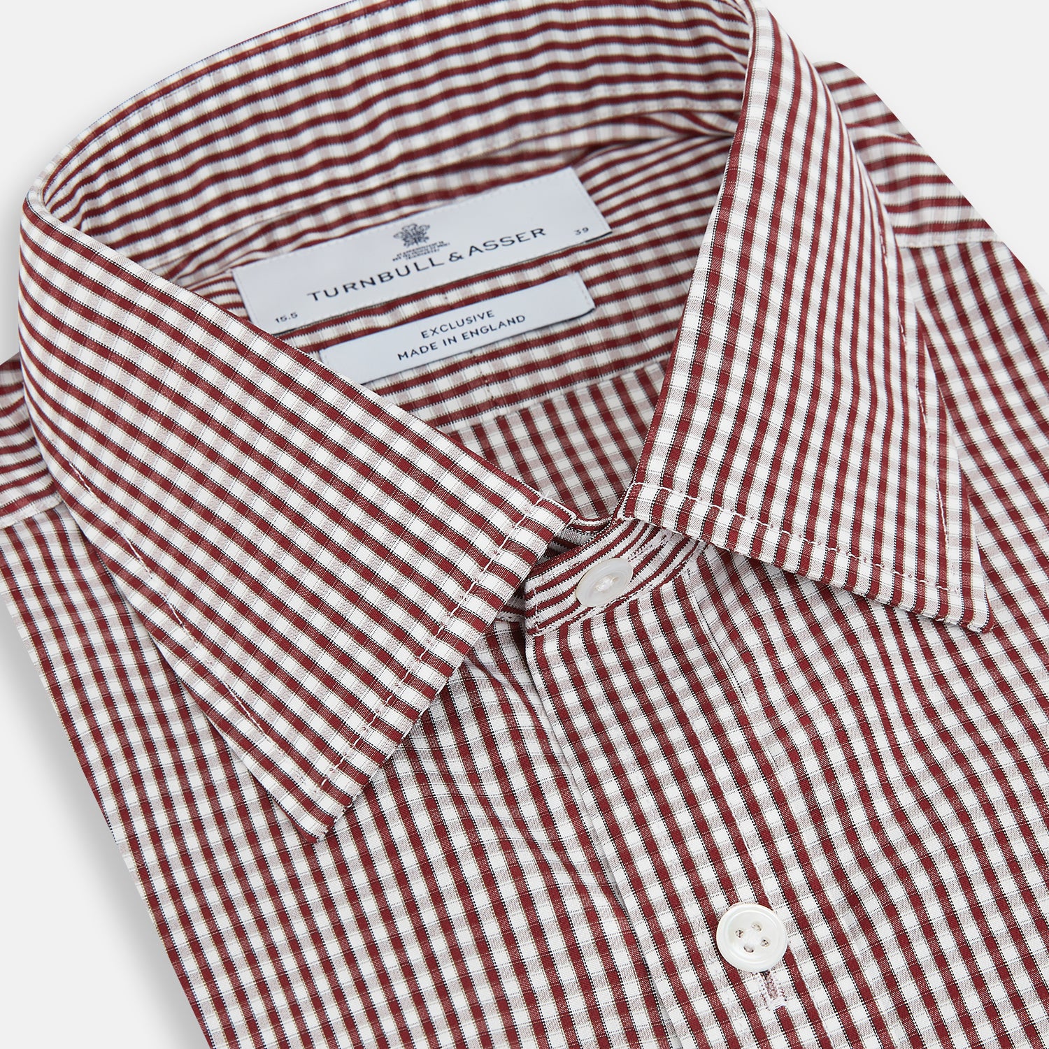 View 2 of product The Turnbull & Asser Burgundy Micro Check Winston Shirt is a long-sleeved, button-up Mayfair fit dress shirt with a collar and buttoned cuffs, featuring a small red and white check pattern and shown on a white background.