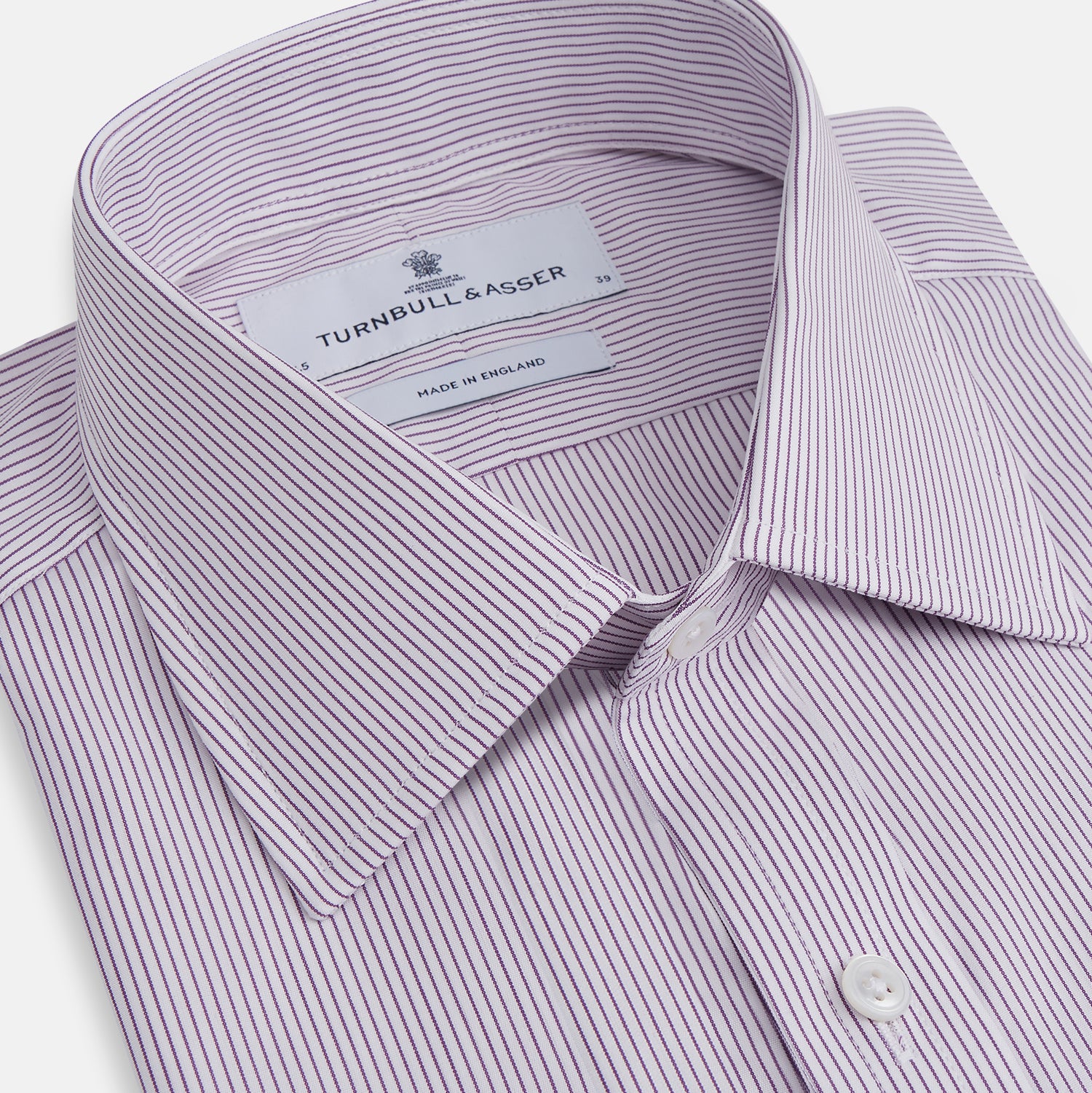 View 2 of product The Purple Pinstripe Mayfair Shirt by Turnbull & Asser is a light purple cotton poplin long-sleeve button-up with white stripes, a pointed collar, white buttons, and cuffed sleeves, shown laid flat on a white background.