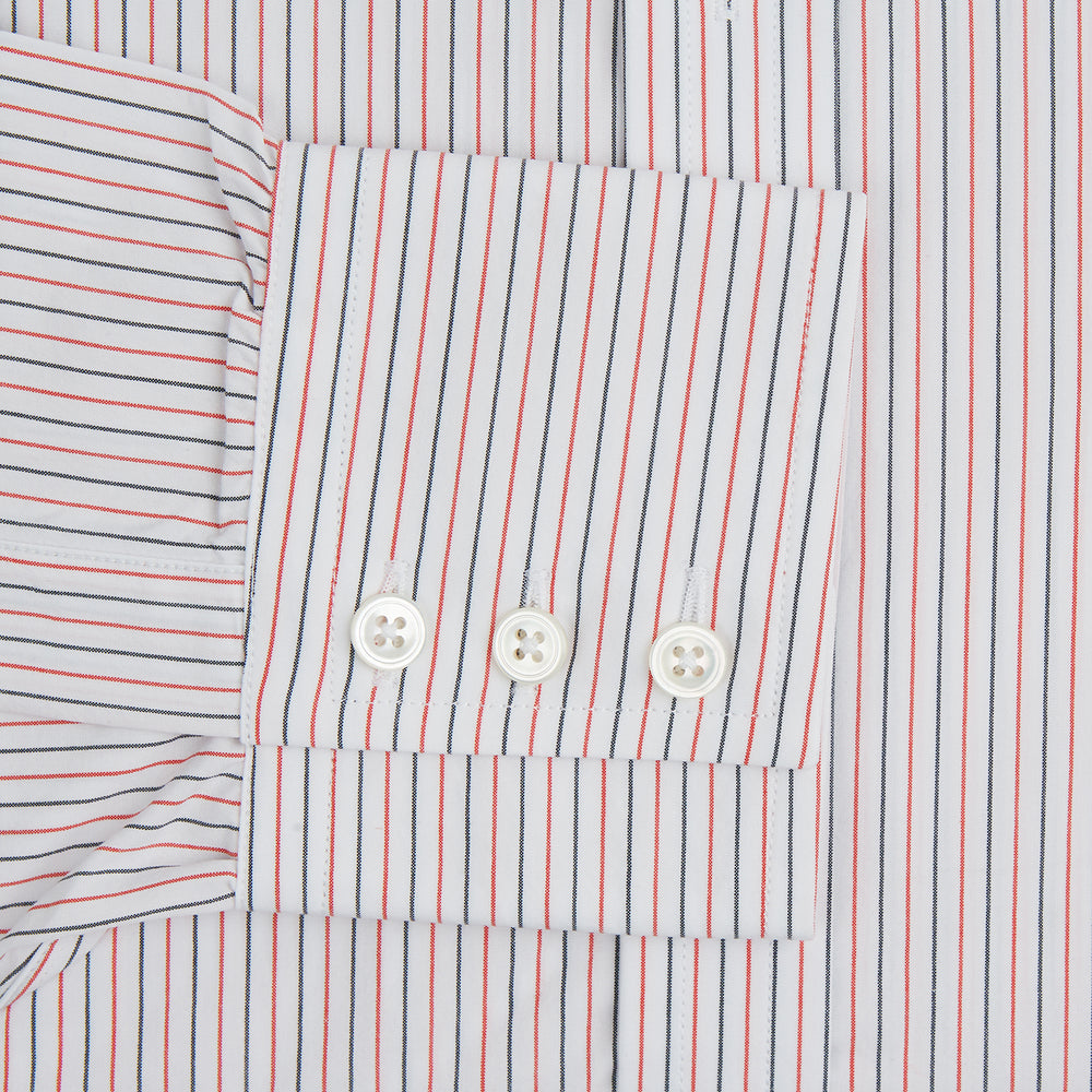The Turnbull & Asser Red and Navy Pinstripe Mayfair Shirt, an organic cotton long-sleeve button-up with a collar, features thin vertical red and navy pinstripes on white, shown laid flat on a white surface.