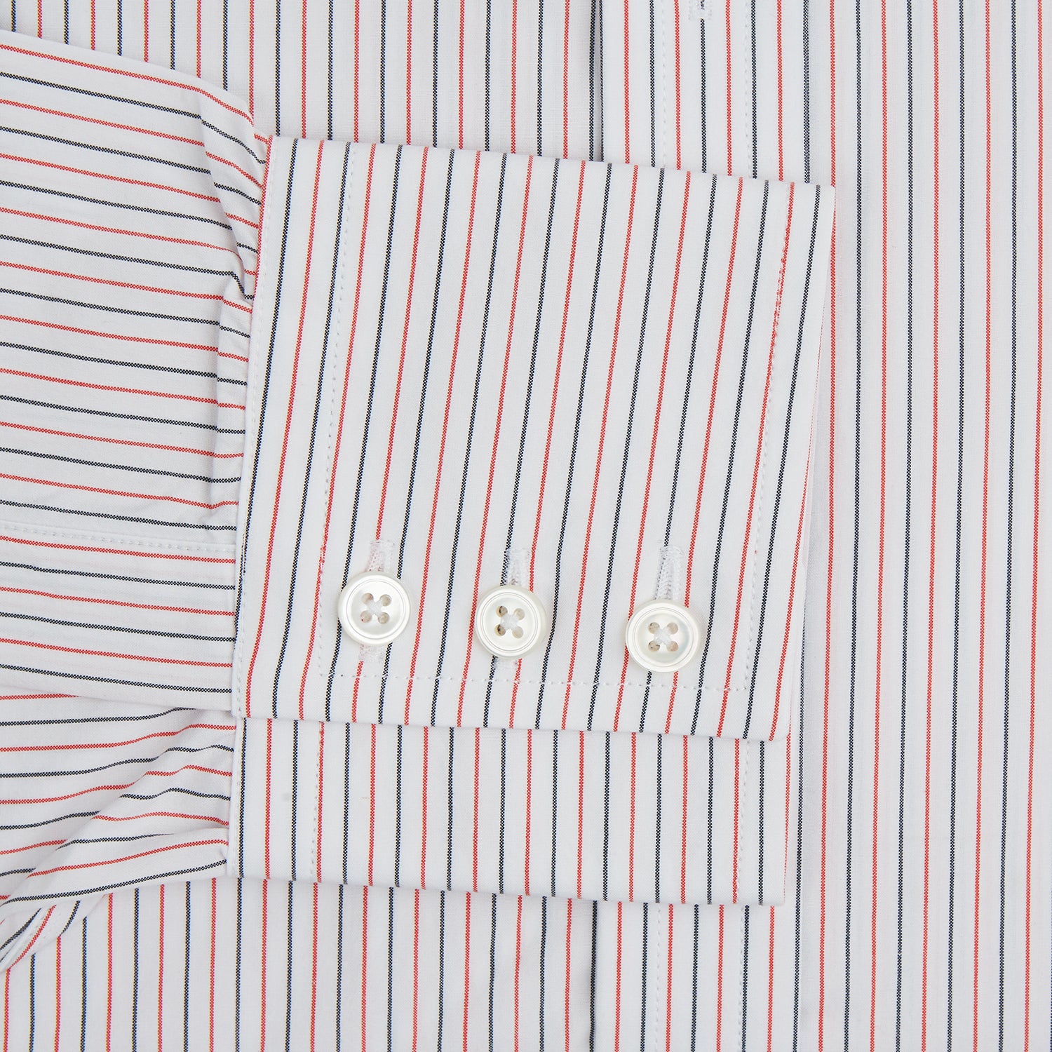 View 3 of product The Turnbull & Asser Red and Navy Pinstripe Mayfair Shirt, an organic cotton long-sleeve button-up with a collar, features thin vertical red and navy pinstripes on white, shown laid flat on a white surface.