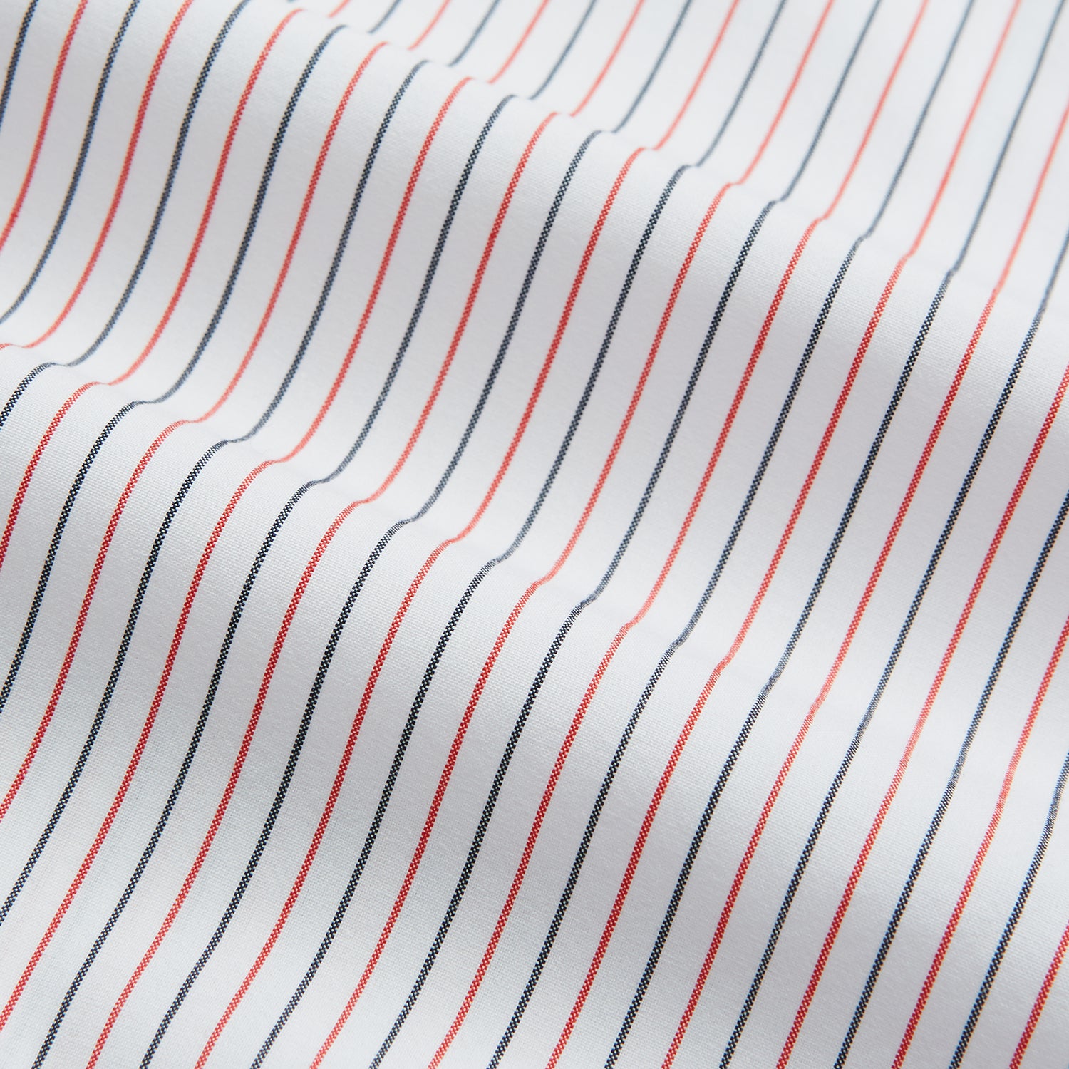 View 5 of product The Turnbull & Asser Red and Navy Pinstripe Mayfair Shirt, an organic cotton long-sleeve button-up with a collar, features thin vertical red and navy pinstripes on white, shown laid flat on a white surface.