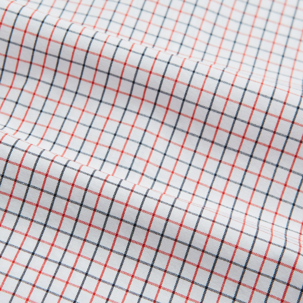 The Turnbull & Asser Red and Navy Graph Check Mayfair Shirt is a long-sleeved organic cotton button-up featuring a collar, buttoned cuffs, and a small red and navy check pattern, shown against a plain white background.