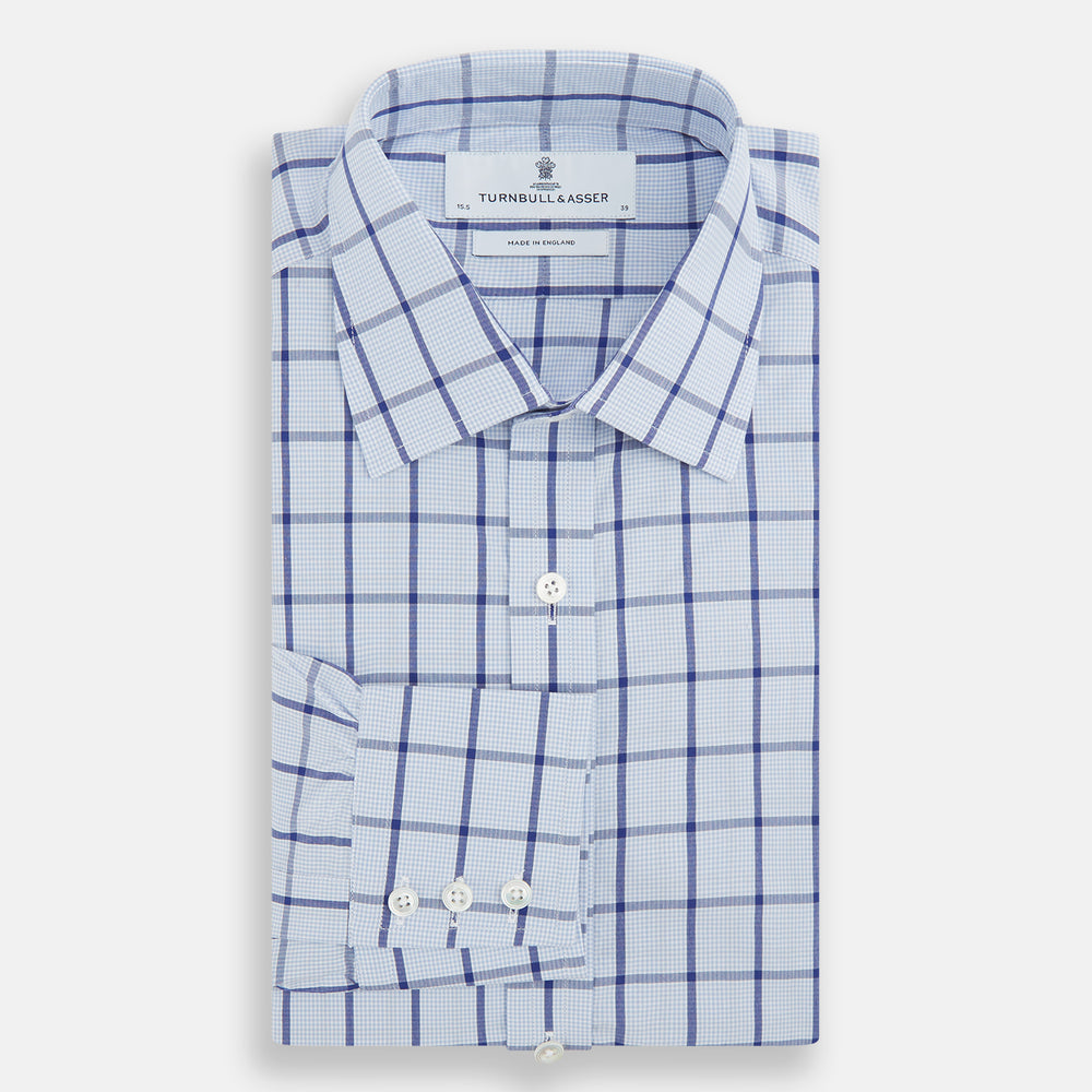 The Turnbull & Asser Navy Blue Windowpane Check Mayfair Shirt is a long-sleeved, organic cotton, button-up dress shirt with a classic collar and buttoned cuffs—white fabric with navy windowpane checks, ideal for any wardrobe capsule.