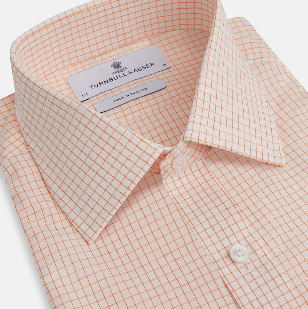 The Turnbull & Asser Orange Graph Check Mayfair Shirt features a classic T&A collar, long sleeves, buttoned cuffs, and a peach and white check pattern, shown against a white background.