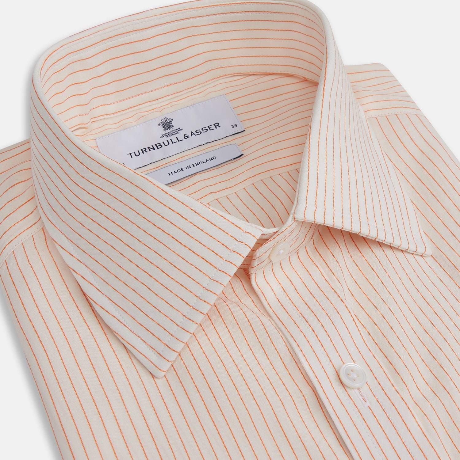 View 2 of product The Turnbull & Asser Orange Pinstripe Mayfair Shirt with a T&A collar and thin peach and white stripes is laid flat on a white background.
