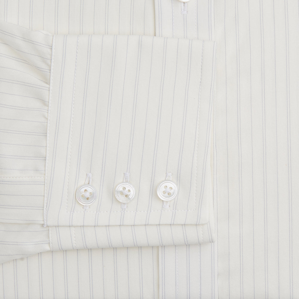 The Turnbull & Asser Pale Blue Fine Track Stripe Mayfair Shirt is a long-sleeve, cream-colored organic cotton shirt with subtle pale blue stripes, a T&A collar, and buttoned cuffs, shown on a plain white background.