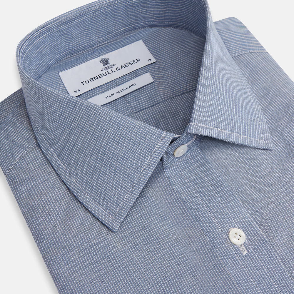 The Turnbull & Asser Blue Pencil Stripe Mayfair Shirt is crafted from organic cotton with a classic collar, white buttons, and buttoned cuffs. Shown laid flat on a white background.