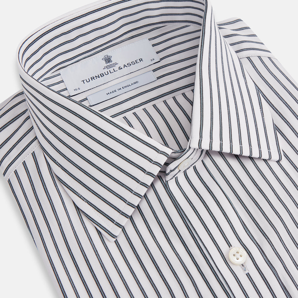 The Turnbull & Asser Midnight Blue Halo Stripe Mayfair Shirt features breathable cotton with black and white vertical stripes, a pointed T&A collar, and buttoned cuffs, displayed flat on a white background.