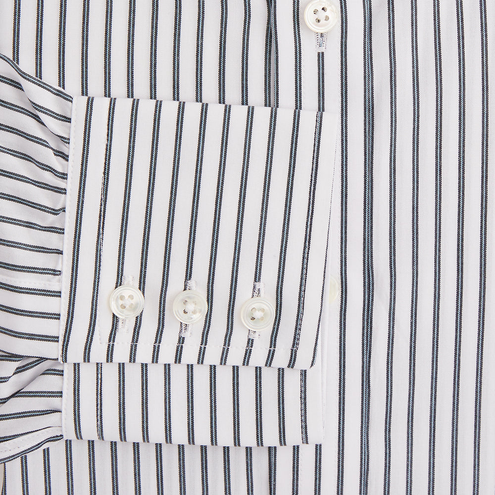 The Turnbull & Asser Midnight Blue Halo Stripe Mayfair Shirt features breathable cotton with black and white vertical stripes, a pointed T&A collar, and buttoned cuffs, displayed flat on a white background.